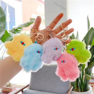Five colorful fluffy plush doll keychains with gold hardware held in hand outdoors