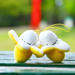 Cute plush peeled banana charms with facial expressions on a green wooden bench outdoors
