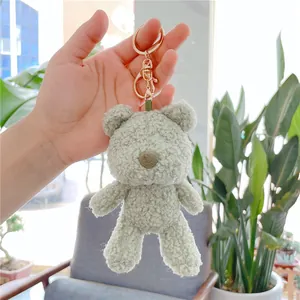 Close-up of mint green plush bear keychain with golden ring held by hand