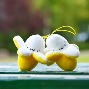 Cute pair of plush banana person keychains with embroidered faces on a green wooden table