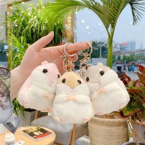Tre portachiavi a forma di criceto in peluche rosa, marrone e grigio tenuti in mano