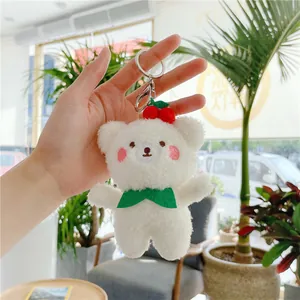 Close-up of white plush bear keychain with cherry decor and green bowtie in hand