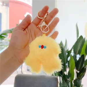 Close-up of yellow fluffy monster plush keychain with gold metal clasp held in hand
