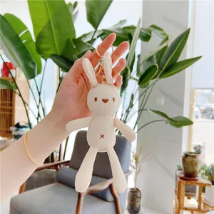 Cute white plush bunny keychain accessory held by hand in a modern living room