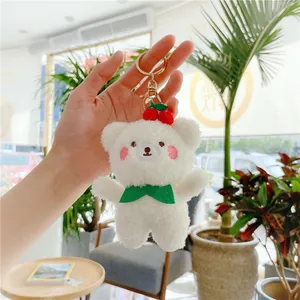 Close-up of white plush bear keychain with green scarf, red cherries and gold clasp