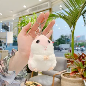 Dettaglio di un portachiavi a forma di criceto in peluche rosa e bianco tenuto in mano