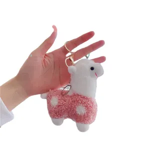 Cute pink and white plush alpaca keychain with golden metal ring held in hand