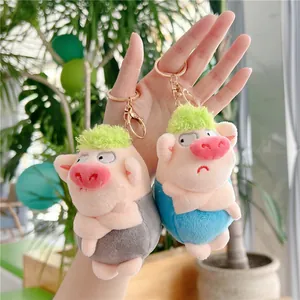 Funny green-haired pig plush keychains in blue and grey outfits shown in hand