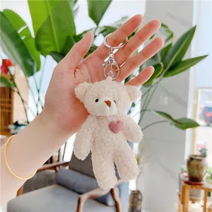 Detail of cream teddy fleece bear keychain with pink heart held by a hand