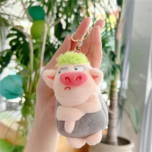 Close-up of pink pig plush keychain with green hair held in hand for size context
