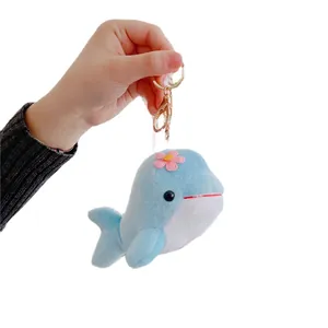 Cute light blue plush dolphin keychain with a pink flower held in hand on white background