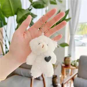 Close-up of white plush teddy bear keychain with black heart held by hand