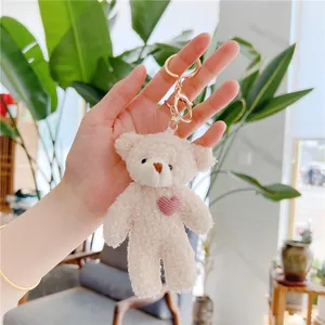 Close-up of beige teddy bear plush keychain with pink heart and golden buckle detail
