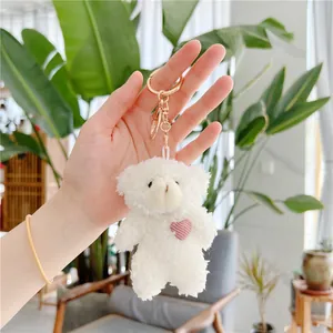 Close-up of white plush bear pendant with pink heart knit and golden metal keychain
