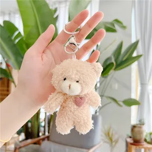 Cute teddy bear plush keychain with pink heart embroidery held in hand for bag decoration