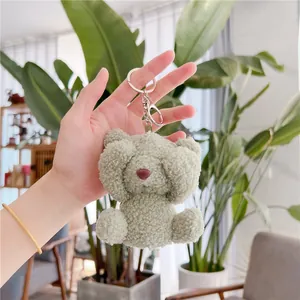 Close-up of sage green curly plush teddy bear pendant with metal keychain held by hand