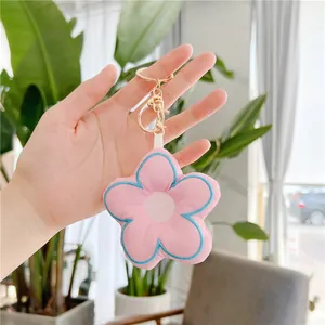 Close-up of pink plush flower keychain with blue embroidery and gold metal clasp