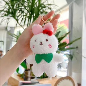 Close-up of a white plush bunny keychain with green bow tie and golden ring hook