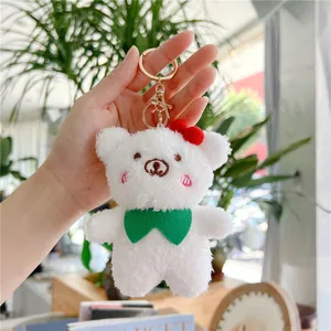 Close-up of white plush bear keychain with green bow tie and pink embroidered cheeks