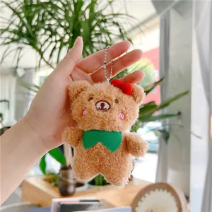 Close-up of a curly brown plush bear keychain with red bow and green necktie held in hand