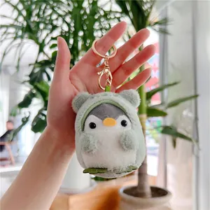 Close-up of cute plush penguin keychain wearing a green frog hoodie held by hand