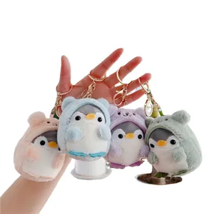 Hand holding four cute penguin plush keychains in colorful animal hoodies