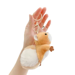 Plush squirrel keychain with brown and white fur held in hand for size visualization