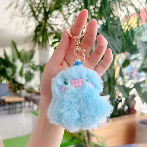 Close-up of blue plush monster keychain with pink embroidery and gold metal hardware
