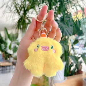 Close-up of yellow plush monster keychain with golden metal hook held in hand