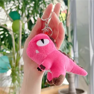 Pink plush dinosaur keychain with silver metal clasp shown held in hand for size