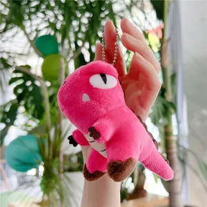 Close-up of pink plush dinosaur keychain held outdoors with green leaf background