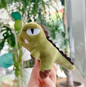 Close-up of a mini bean green dinosaur plush keychain held by hand in a soft lighting