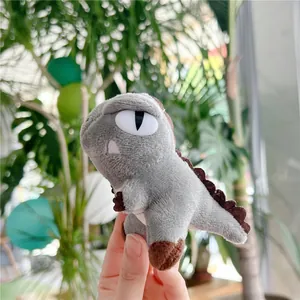 Detail shot of a small grey plush dinosaur keychain held in hand against green leaves