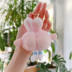 Detail of pink plush rabbit keychain with funny peach butt design held against plants