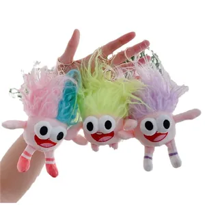 Three colorful fuzzy monster plush keychains with bulging eyes held by hand on white background