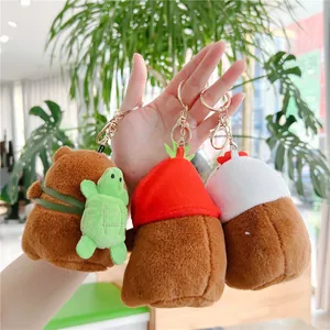 Three plush capybara keychains with turtle, strawberry, and chick hats held by hand