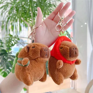 Detail of plush capybara keychains in green turtle shell and red strawberry outfits