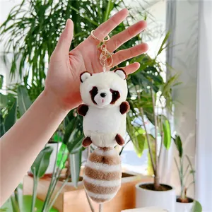 Close-up of cute plush raccoon keychain with striped tail held in hand and metal clasp
