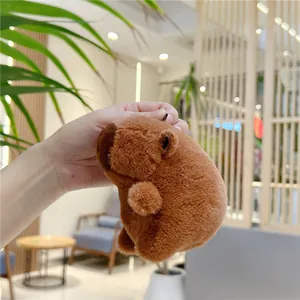 Gros plan d'un porte-clés capybara en peluche marron tenu à la main dans un décor chaleureux