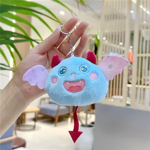 Gros plan d'un porte-clés monstre en peluche bleue avec ailes roses tenu à la main