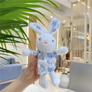 Cute white plush rabbit toy wearing a blue floral dress held in a bright home setting