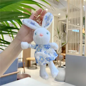 Close-up of cute white plush bunny keychain wearing a blue floral dress and metal clasp