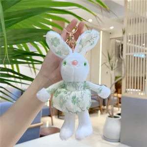 Close-up of a plush white bunny keychain wearing a green floral dress with a gold clasp