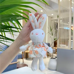 Close-up of a white plush rabbit keychain wearing a cute orange floral dress with a metal clip