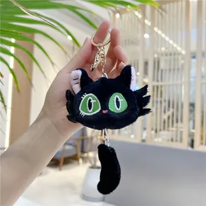 Detail of black plush cat keychain with green embroidered eyes and gold hardware