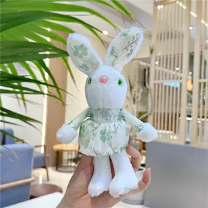 Close-up of a plush white bunny charm wearing a green floral mesh dress in hand