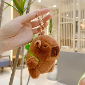 Close-up of cute brown capybara plush toy with a green backpack and golden keychain