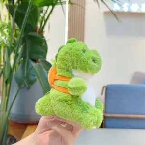 Close-up of green plush dinosaur pendant with orange carrot backpack and soft fur texture