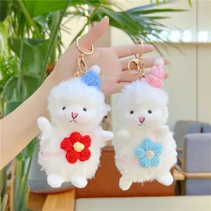 Hand holding two cute plush sheep keychains with blue and pink hats on a bright background