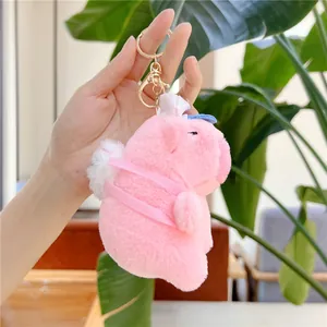 Pink Capybara plush keychain with blue hat and golden metal clip shown in hand